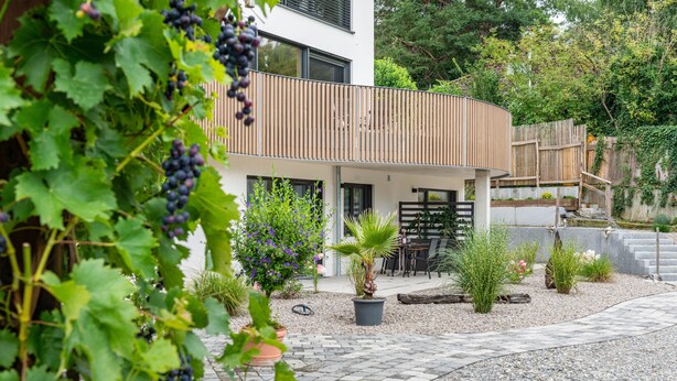Una casa moderna con balcón, plantas en macetas y un camino de grava.