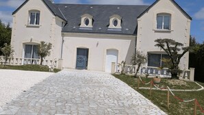 En toetages bygning med en symmetrisk facade, en midterliggende indgang med en blå dør og en brostensbelagt indkørsel der fører til indgangen.