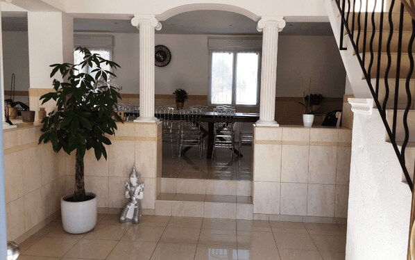 A spacious dining area with a high ceiling, columns, and a staircase.