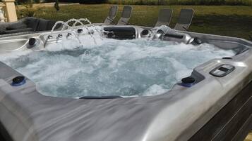 A hot tub with multiple jets, a control panel, and a seating area with lounge chairs.