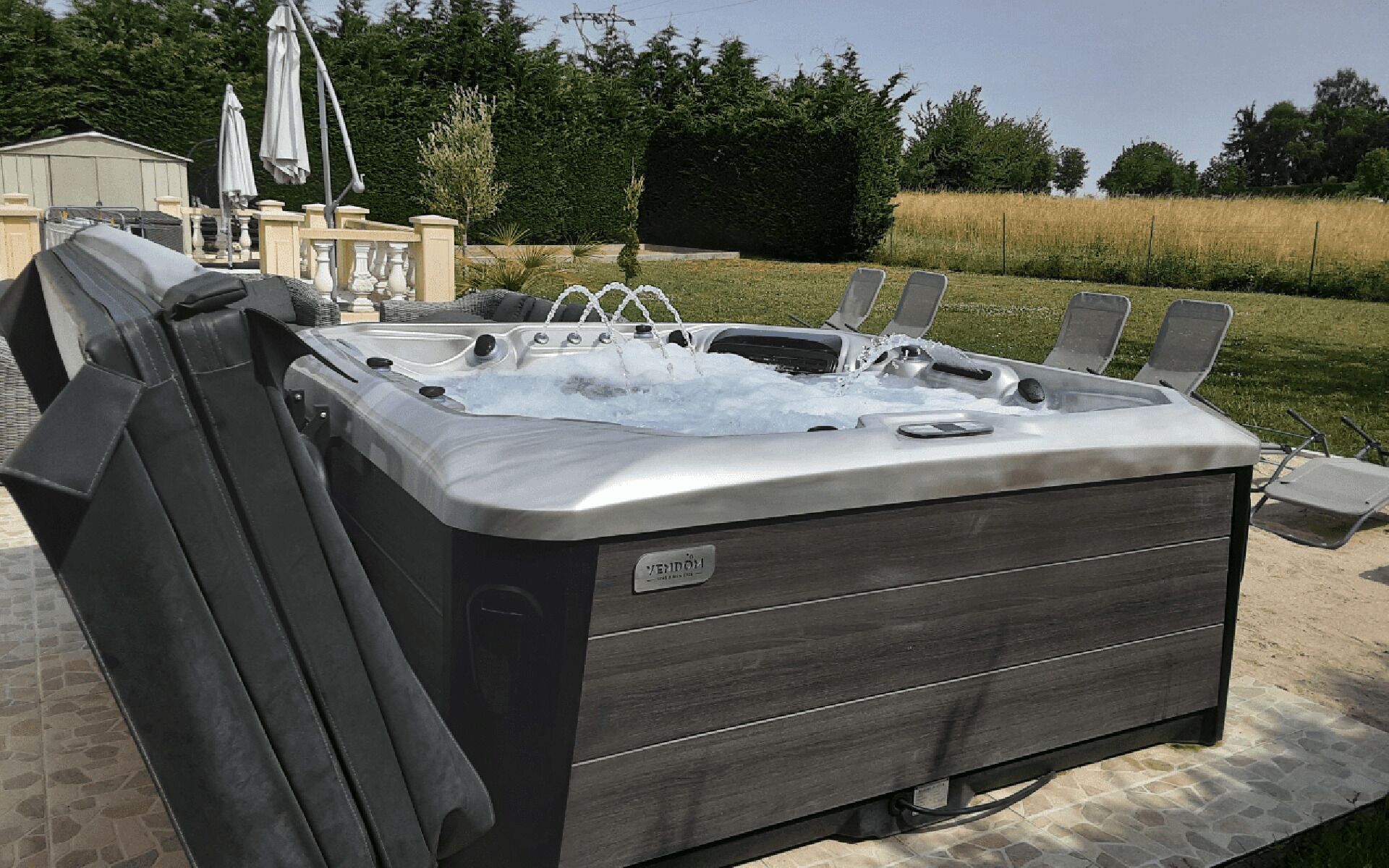 Un bain à remous doté d’un siège intégré, situé à l’extérieur, sur une terrasse dont le sol est en pierre.