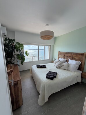 A bedroom with a large bed, a wooden headboard, a window with a view of the sea, and a potted plant. - Apartment "Sur l'Eau" walking distance to beach and center. Gulf of Saint-Tropez (Sainte-Maxime)