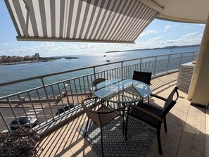 A balcony with a glass table and chairs, overlooking a body of water with boats and a distant shoreline. - Apartment "Sur l'Eau" walking distance to beach and center. Gulf of Saint-Tropez (Sainte-Maxime)