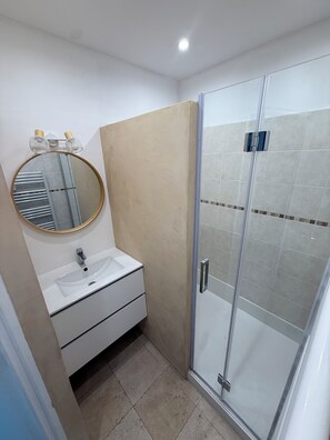 A bathroom with a white sink, a round mirror, and a glass shower enclosure. - Apartment "Sur l'Eau" walking distance to beach and center. Gulf of Saint-Tropez (Sainte-Maxime)