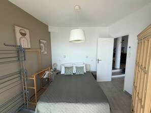 Een slaapkamer met een bed, een nachtkastje, een lamp, een kledingkast en een deur naar een andere kamer.