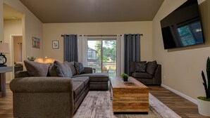 A modern living room with a sectional sofa, a wooden coffee table, and a large TV mounted on the wall. - Modern Mountain Home w/ Hot Tub, Fenced Yard & Near Lakes (Pagosa Springs)