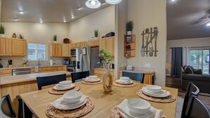 A modern kitchen with wooden cabinets, stainless steel appliances, and a dining area set for six with woven placemats. - Modern Mountain Home w/ Hot Tub, Fenced Yard & Near Lakes (Pagosa Springs)
