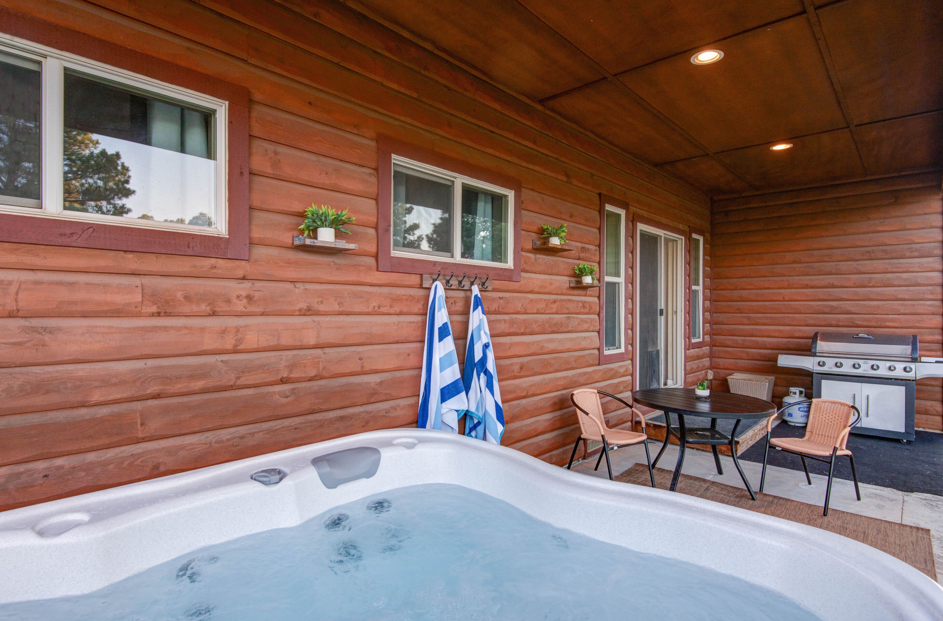 A wooden cabin with a hot tub, a table with chairs, and a grill area.