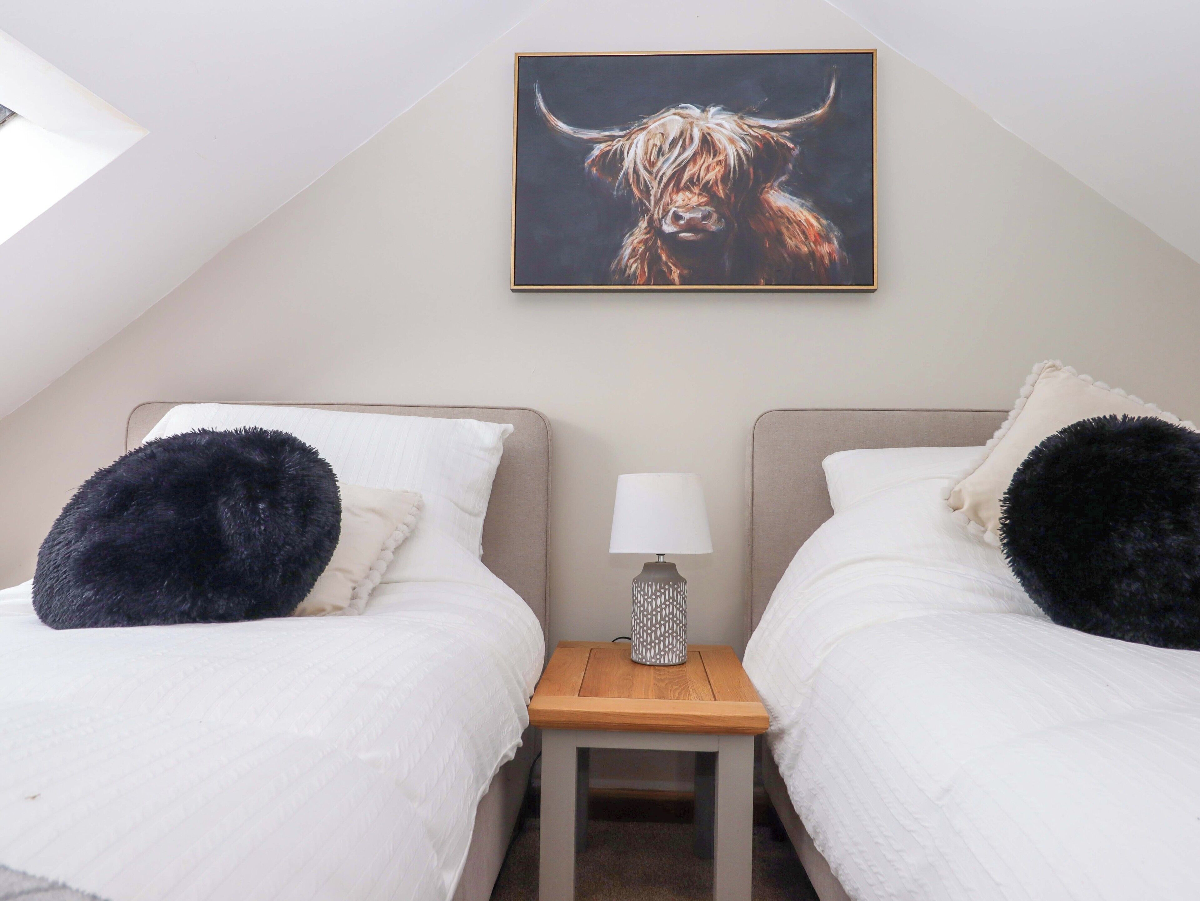 Een slaapkamer met twee bedden, een nachtkastje, een lamp en een schilderij van een stier aan de muur.