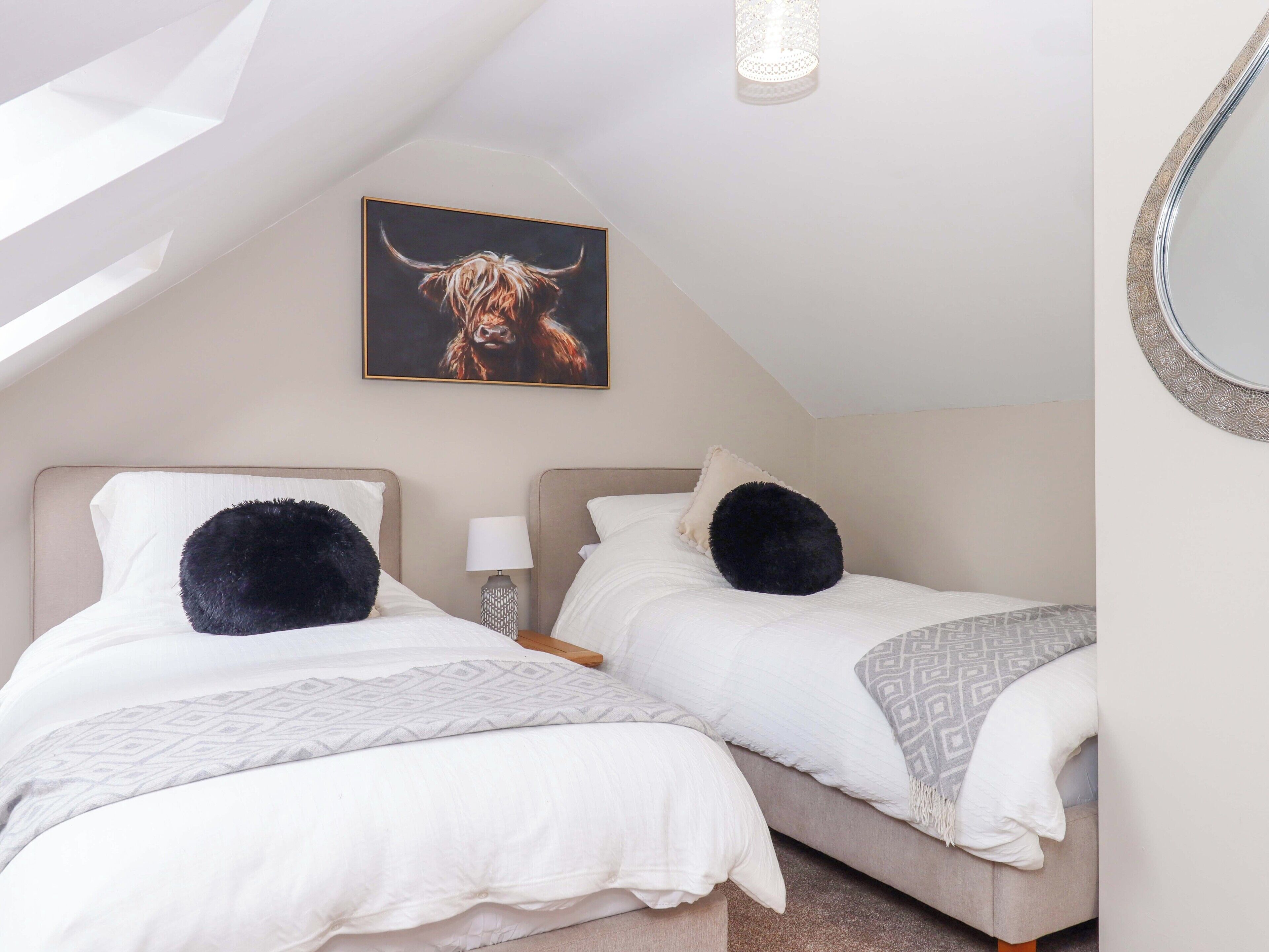 Ein Schlafzimmer mit zwei Betten, einer Deckenleuchte, einem wandmontierten Spiegel und einem Gemälde eines Stiers.