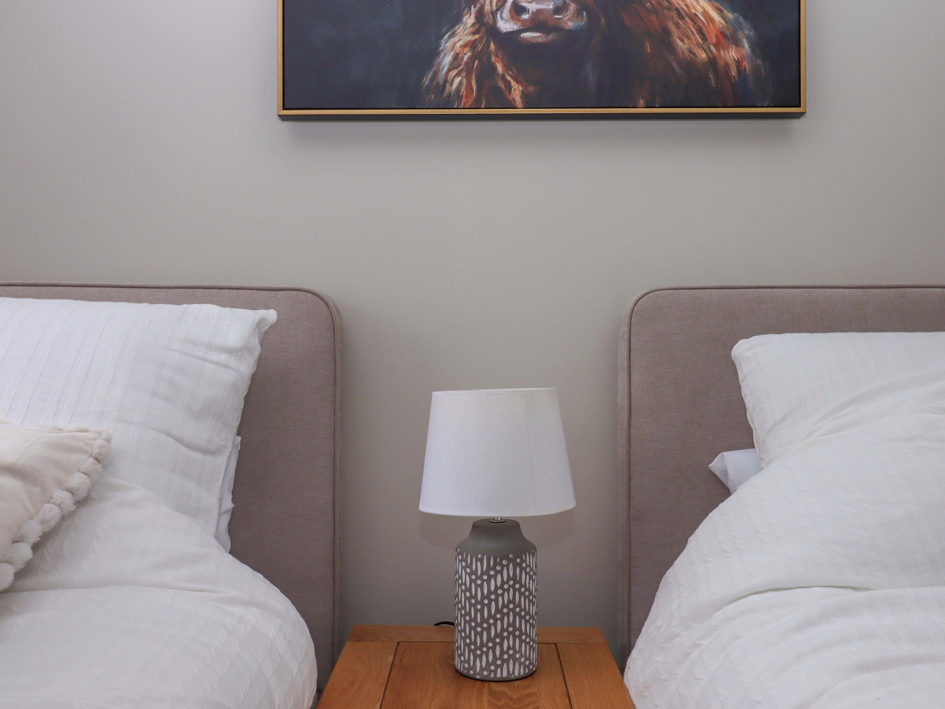 Ein Hotelzimmer mit zwei Betten, einem Nachttisch mit Lampe und einem gerahmten Bild an der Wand.