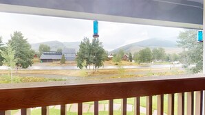 Vista desde un balcón con barandilla de madera, sobre una zona residencial con casas y árboles, y una cordillera al fondo.