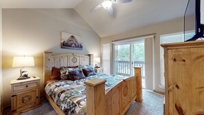 Un dormitorio con cama de madera, una mesita de noche con lámpara, un armario de madera, un ventilador de techo y un ventanal con persianas.