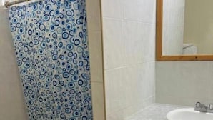 Un baño con inodoro, cortina de ducha con estampado azul y blanco, lavamanos con espejo y armarios de madera.