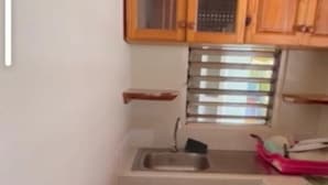 Una cocina compacta con armarios de madera, un lavamanos de acero inoxidable y una ventana con persianas.