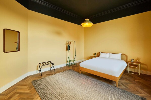 Un dormitorio con una cama grande, una lámpara colgante, un espejo y un taburete pequeño.