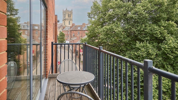 Un balcon avec une table et des chaises, donnant sur une rue et un bâtiment historique.