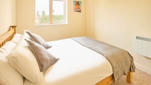 Une chambre à coucher avec un lit, des oreillers, une fenêtre, un radiateur et une œuvre d’art murale.