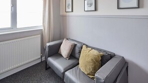 Un canapé en cuir gris avec deux coussins, un radiateur blanc et trois œuvres d’art encadrées accrochées au mur.