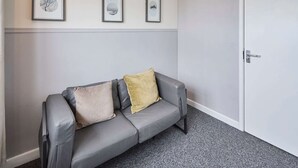 Un canapé en cuir gris avec deux coussins, une porte blanche et trois tableaux encadrés accrochés au mur.