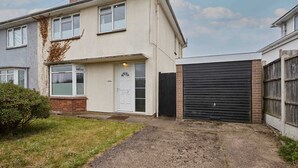 Un immeuble résidentiel de deux étages, doté d’une porte de garage, d’une porte d’entrée et d’un petit jardin à l’avant.