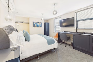 A modern hotel room with a bed, desk, and TV.
