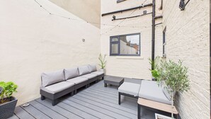 A patio with a grey sofa, a small table, and potted plants.
