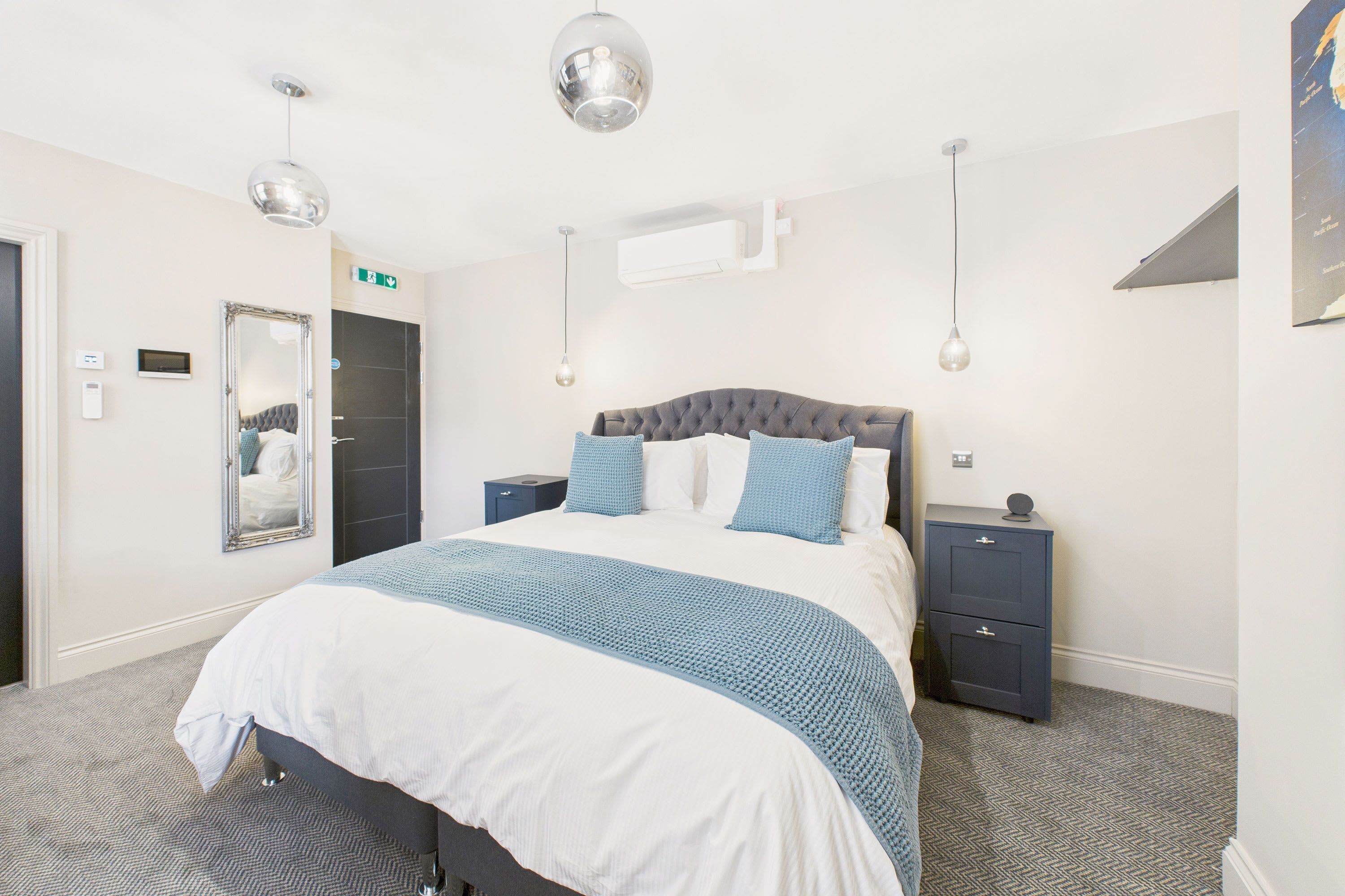 Une chambre d’hôtel moderne avec un grand lit, des tables de chevet, une armoire et un miroir.