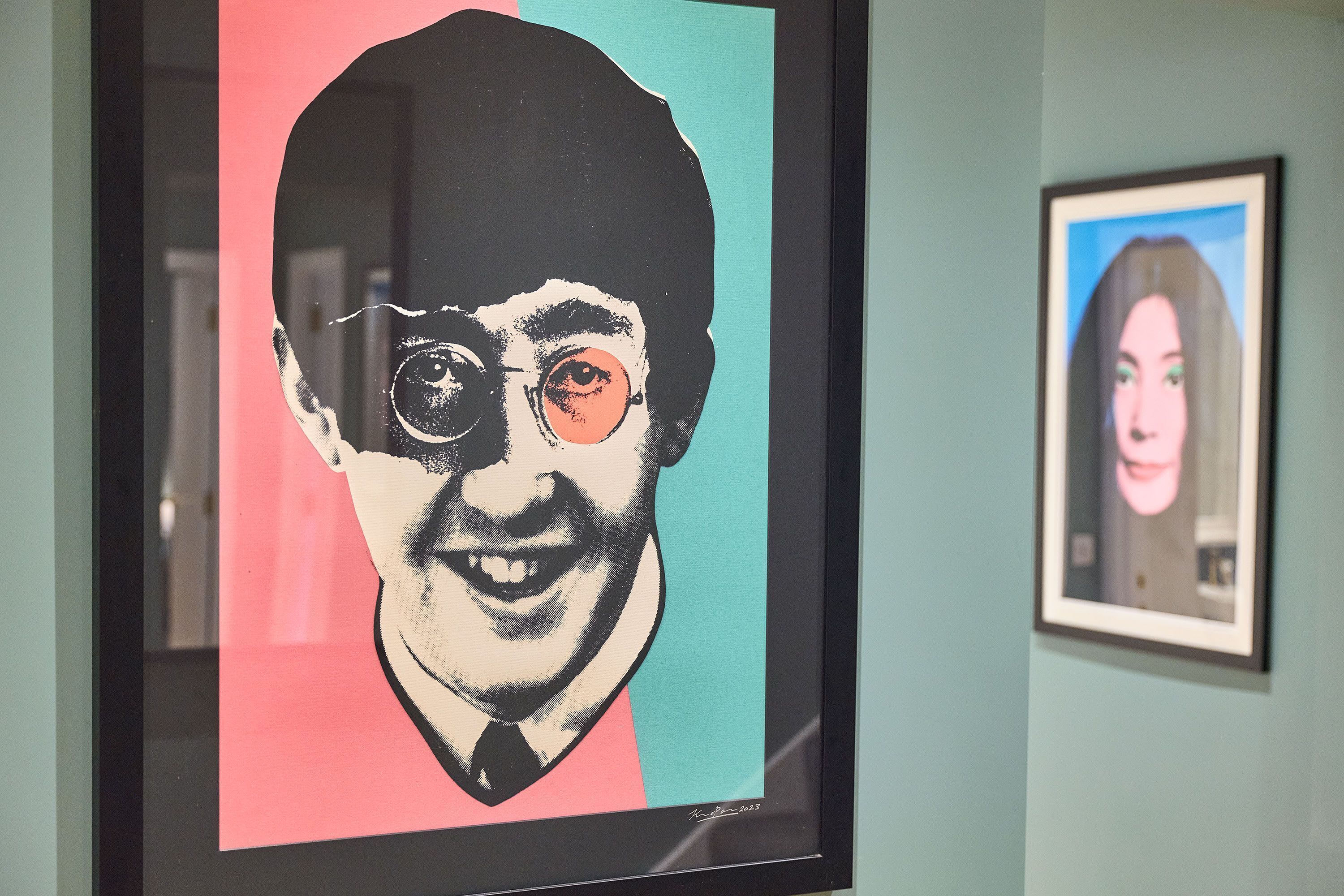 A framed artwork with a partial view of a person's face, a framed picture on the wall, and a teal wall.