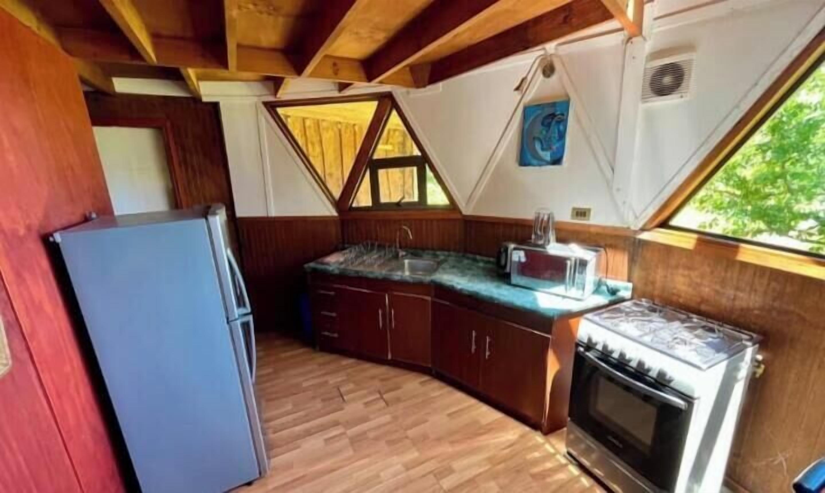 Una cocina funcional con suelo de madera, un refrigerador, una estufa y un ventanal que proporciona luz natural.