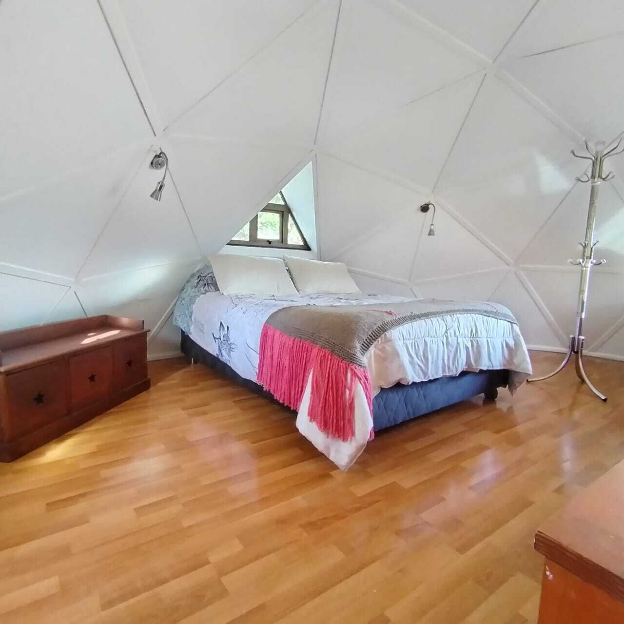 Une chambre avec un plafond en pente, un lit recouvert d’une couvre-lit rose et blanc, une commode en bois et une lampe sur pied.