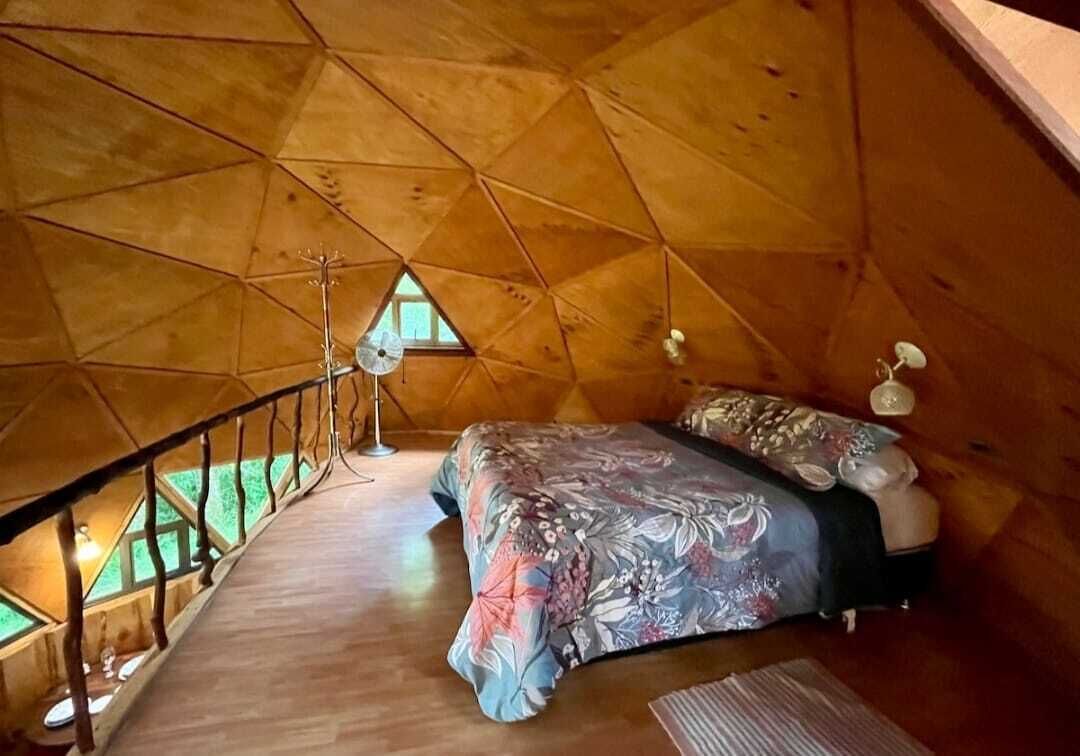 An attic bedroom with a sloped ceiling, a bed with floral bedding, a small window, and a wooden floor.