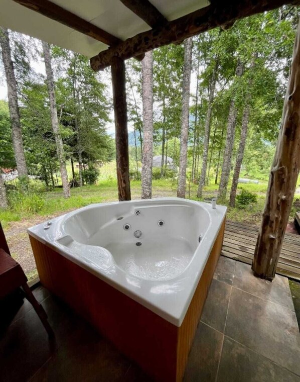 A hot tub in a covered outdoor area with a view of a forest. - Domo Huepil (Pucon)