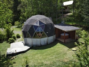 A geodesic dome structure with a central skylight, surrounded by a wooden deck and a hot tub. - Domo Huepil (Pucon)