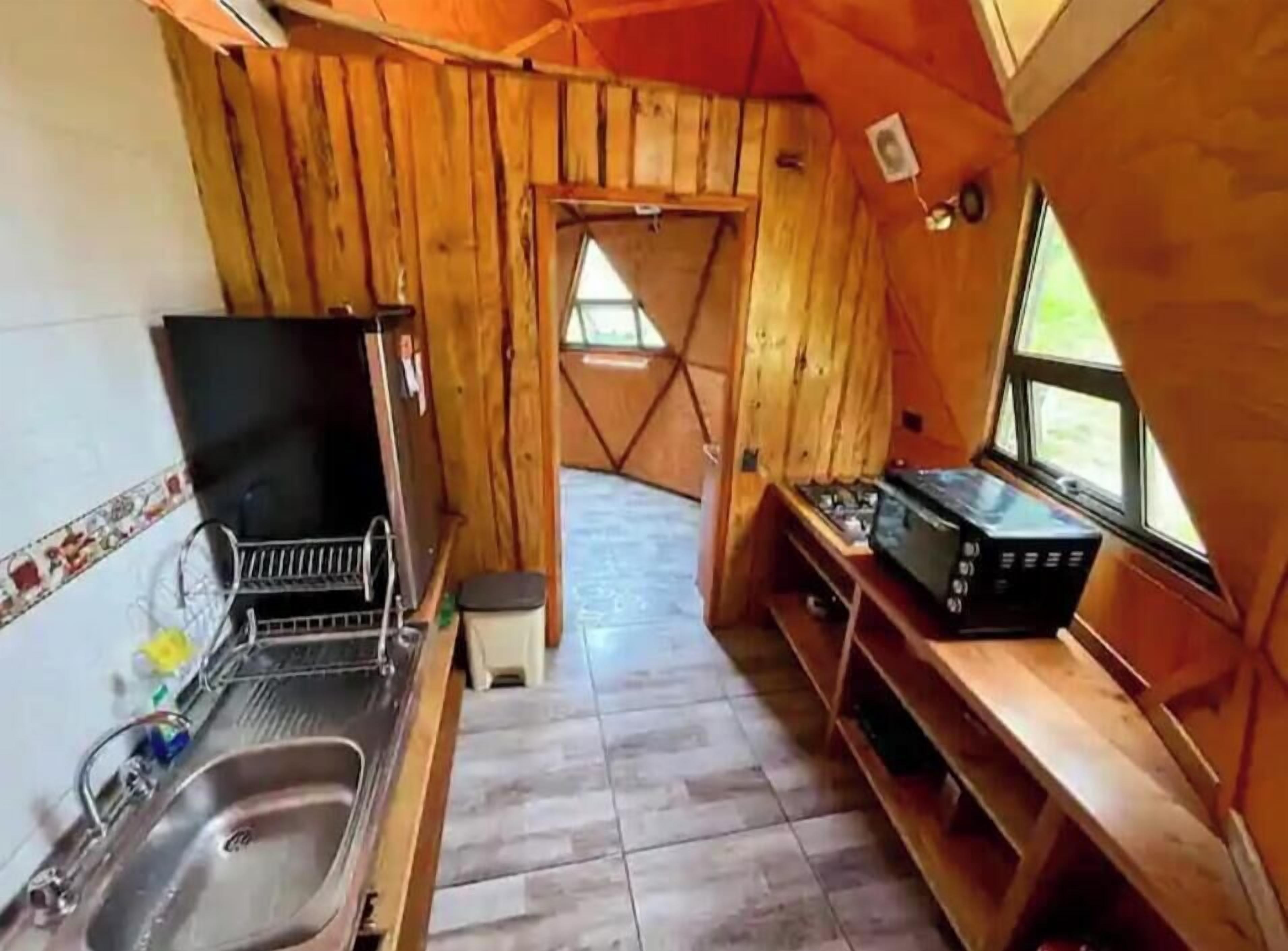 Eine kleine Küche mit Holzwänden, einem Spülbecken, einem Herd und einem Fenster.