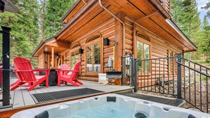 A wooden cabin with a hot tub, red Adirondack chairs, and a deck.
