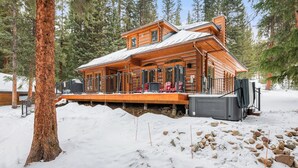 A log cabin with a deck, surrounded by snow and trees.