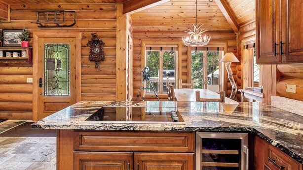 A log cabin kitchen with wooden walls, a marble countertop, and a chandelier.