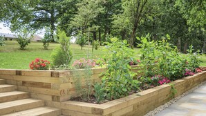 A garden with wooden steps leading to a raised planter bed with various plants and flowers.