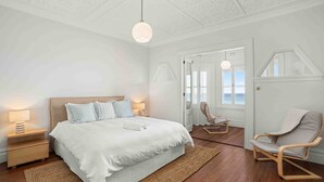 Ein Schlafzimmer mit Bett, Nachttischlampen, einem Sessel und Meerblick durch eine Tür.