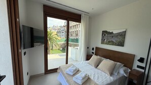 A hotel room with a bed, a TV mounted on the wall, a painting, and a balcony with a view of buildings and a palm tree. - Villa Raquel Montanejos, 12 people, 6 bathrooms, swimming pool, garden, barbecue. (Montanejos)