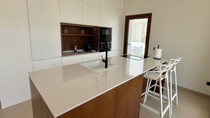 A modern kitchen with a central island, built-in appliances, and a seating area with white chairs. - Villa Raquel Montanejos, 12 people, 6 bathrooms, swimming pool, garden, barbecue. (Montanejos)