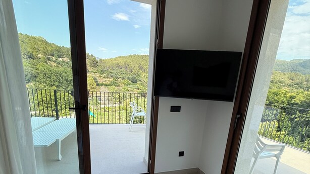 A hotel room with a bed, a TV mounted on the wall, and a balcony with a view of the hills. - Villa Raquel Montanejos, 12 people, 6 bathrooms, swimming pool, garden, barbecue. (Montanejos)