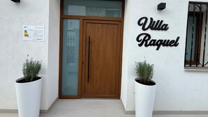 A building entrance with a wooden door, a sign reading "Villa Raquel," and two potted plants. - Villa Raquel Montanejos, 12 people, 6 bathrooms, swimming pool, garden, barbecue. (Montanejos)