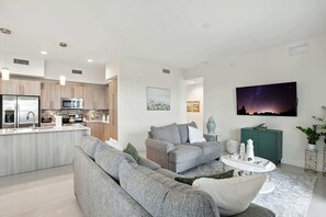 Una sala moderna con un sofá gris, una mesa de centro y una cocina con microondas y lavamanos.