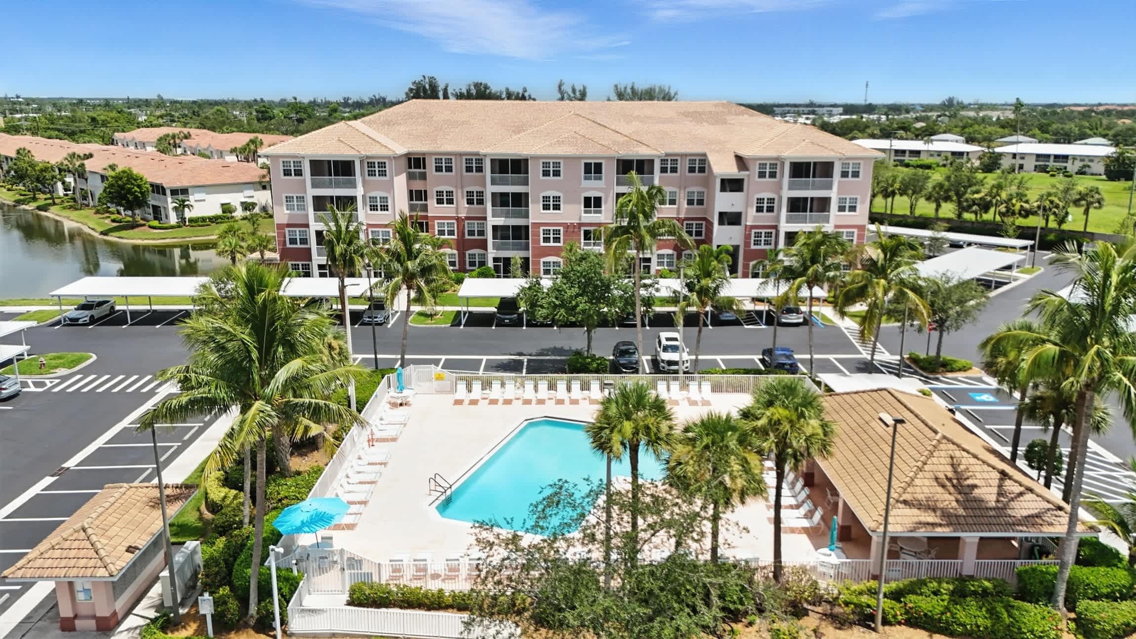 Un hôtel à plusieurs étages doté d’une piscine, d’un parking et de palmiers.