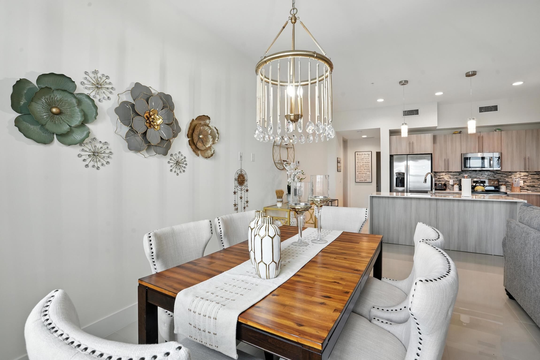 A modern dining area with a wooden table, white upholstered chairs, and a chandelier.