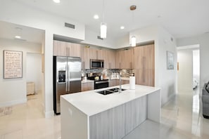 Une cuisine moderne dotée d’un îlot central, d’appareils électroménagers en acier inoxydable et de meubles de rangement en bois.