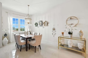 Un espace repas comprenant une table et des chaises, un lustre, des œuvres d’art décoratives au mur et une console sur laquelle sont disposés des vases.