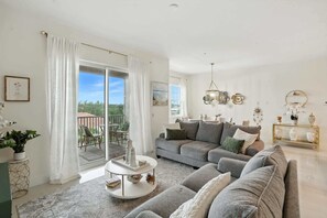 A spacious living room with a grey sofa, a round coffee table, and a balcony with outdoor furniture.